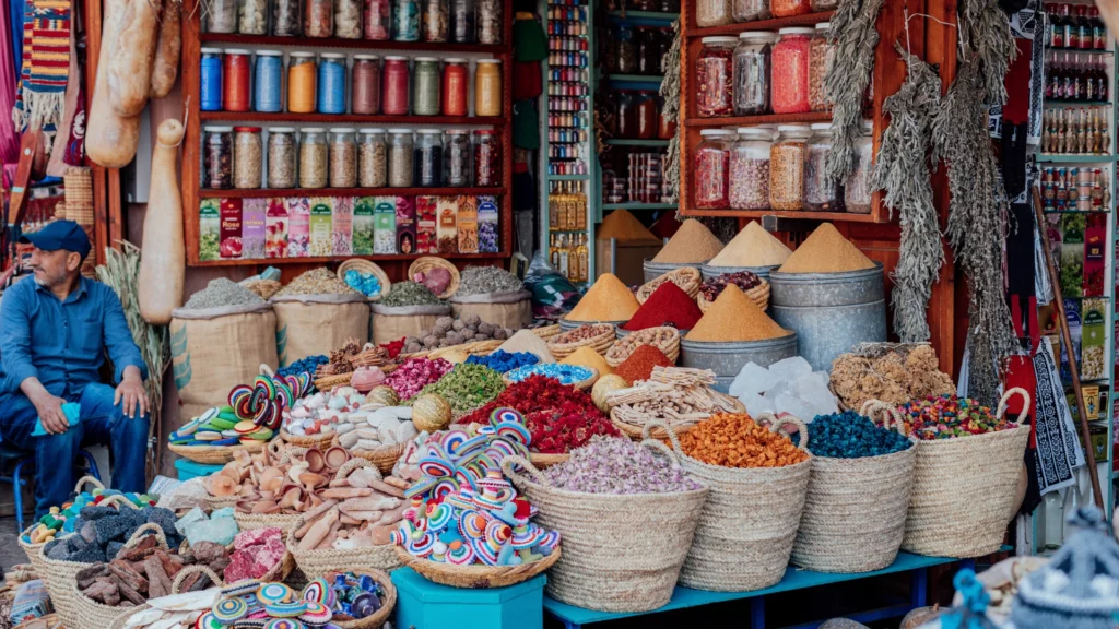 Colorful stalls at Agadir market in Morocco, displaying fresh produce, spices, and local handicrafts with shoppers browsing the vibrant marketplace.